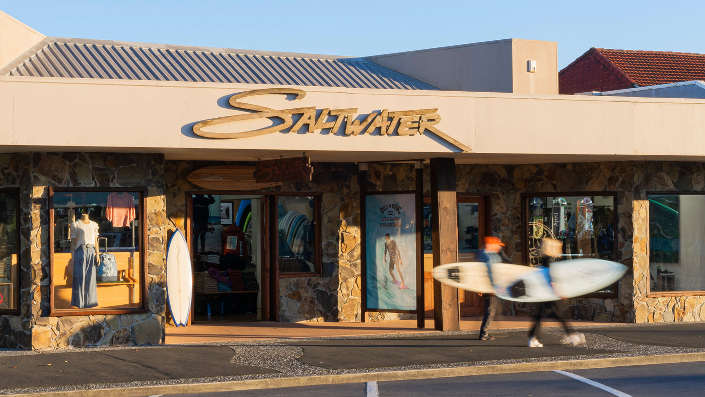 This picture shows the shop front of Saltwater in a nice sunrise light and two people walk past with their saltwater surfboards.