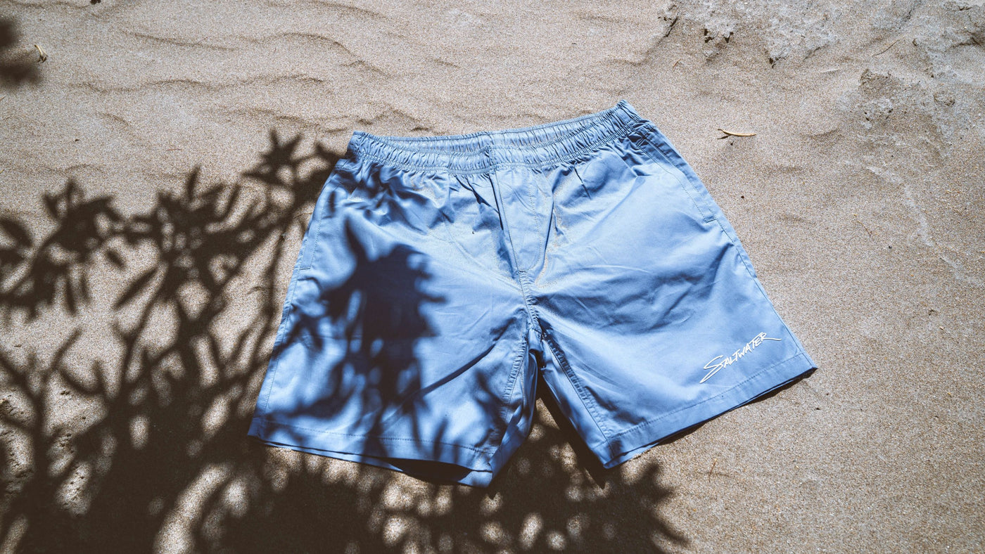 Saltwater Stick Beach Shorts in Carolina Blue laying in the sand on the beach.