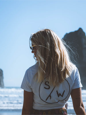 A girl on the beach somewhere on the South Island, wears a white saltwater sketch tee.